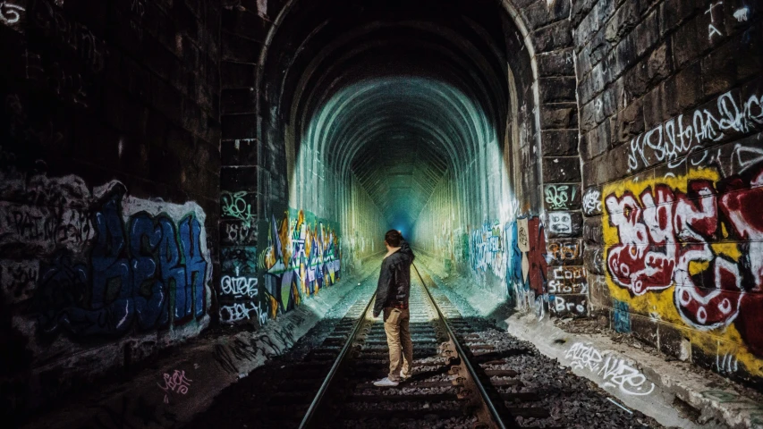 the man is walking through the tunnel covered in graffiti