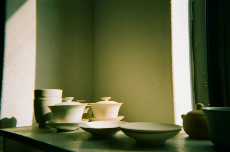 small white bowls and plates are stacked in front of the window