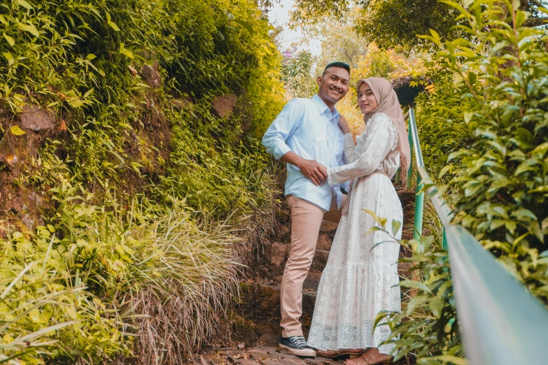 a couple poses for the camera on a set of stairs surrounded by trees