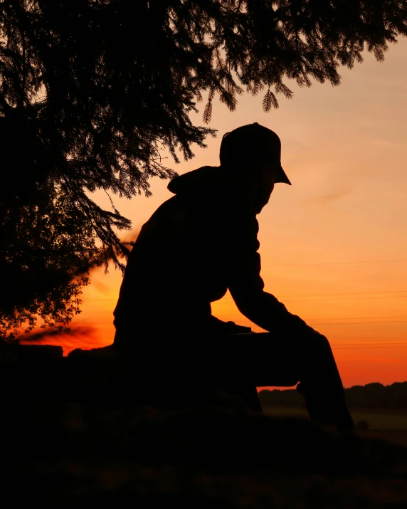 a silhouette picture of a man sitting under a tree
