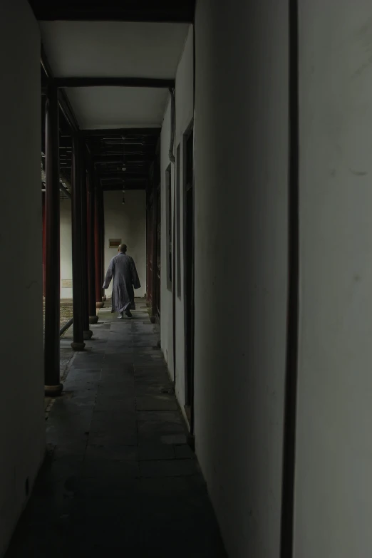 a man in black coat walking down a hall way