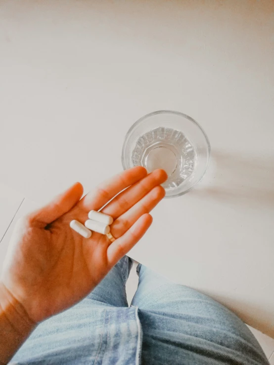 a person holds a cup and pills in their hand