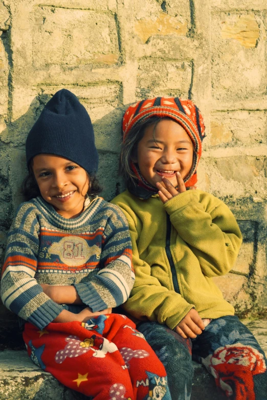 two young children sitting on a ledge and smiling