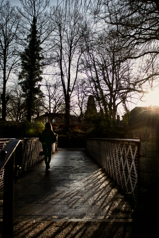 a person walking across a bridge with the sun shining on them
