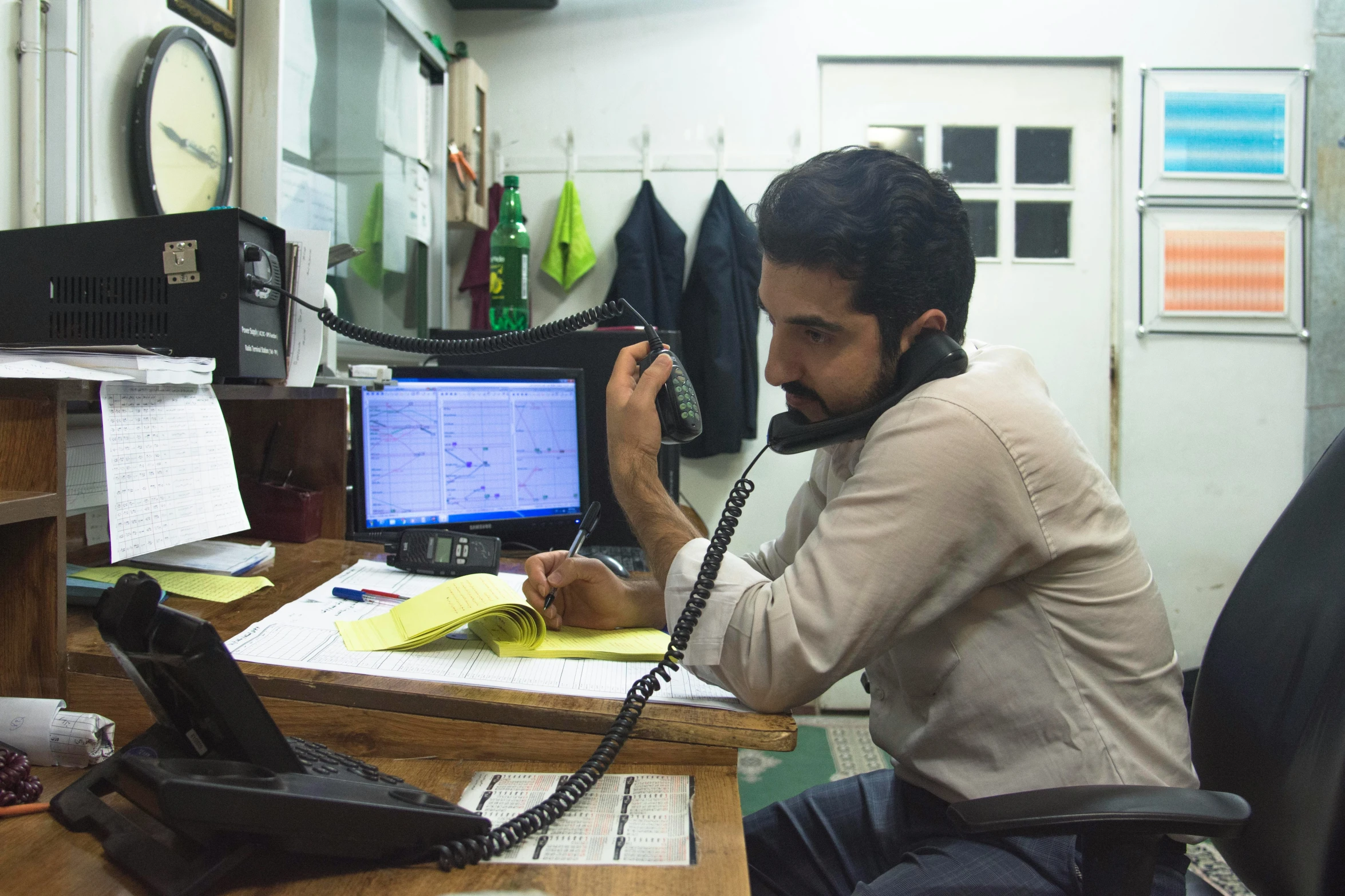 a man on a cell phone with paperwork and laptop at his desk