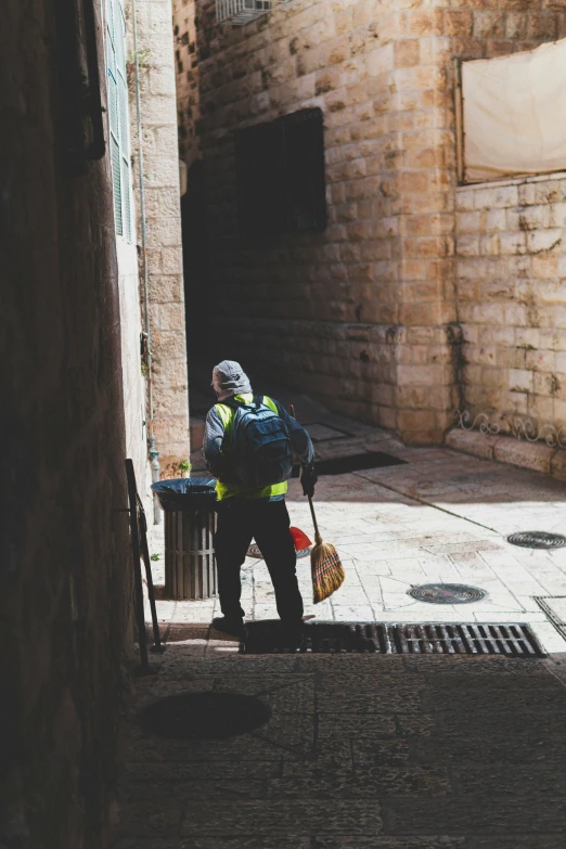 a man in a vest carrying a broom and garbage can