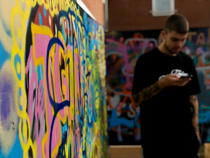 a man standing next to colorful graffiti writing on his cell phone