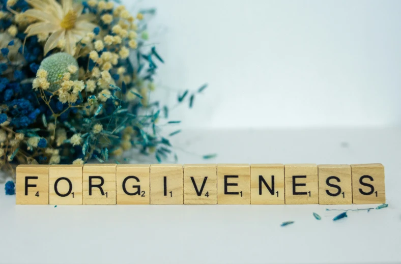 a scrabble type word on a wooden block that says forgivenses next to flowers