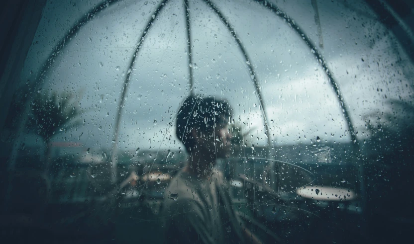 a person standing outside looking out a window at the rain