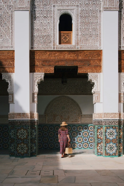 a person with a hat walking on the sidewalk next to a large wall