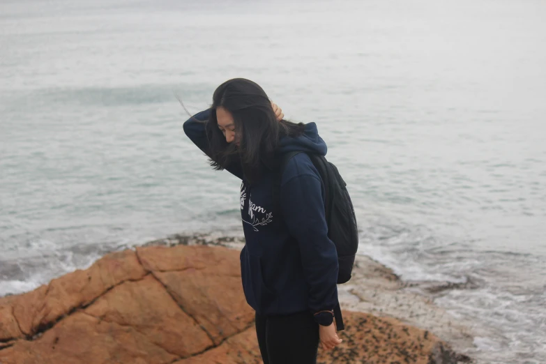 a young man stands near the ocean and looks down at the rocks