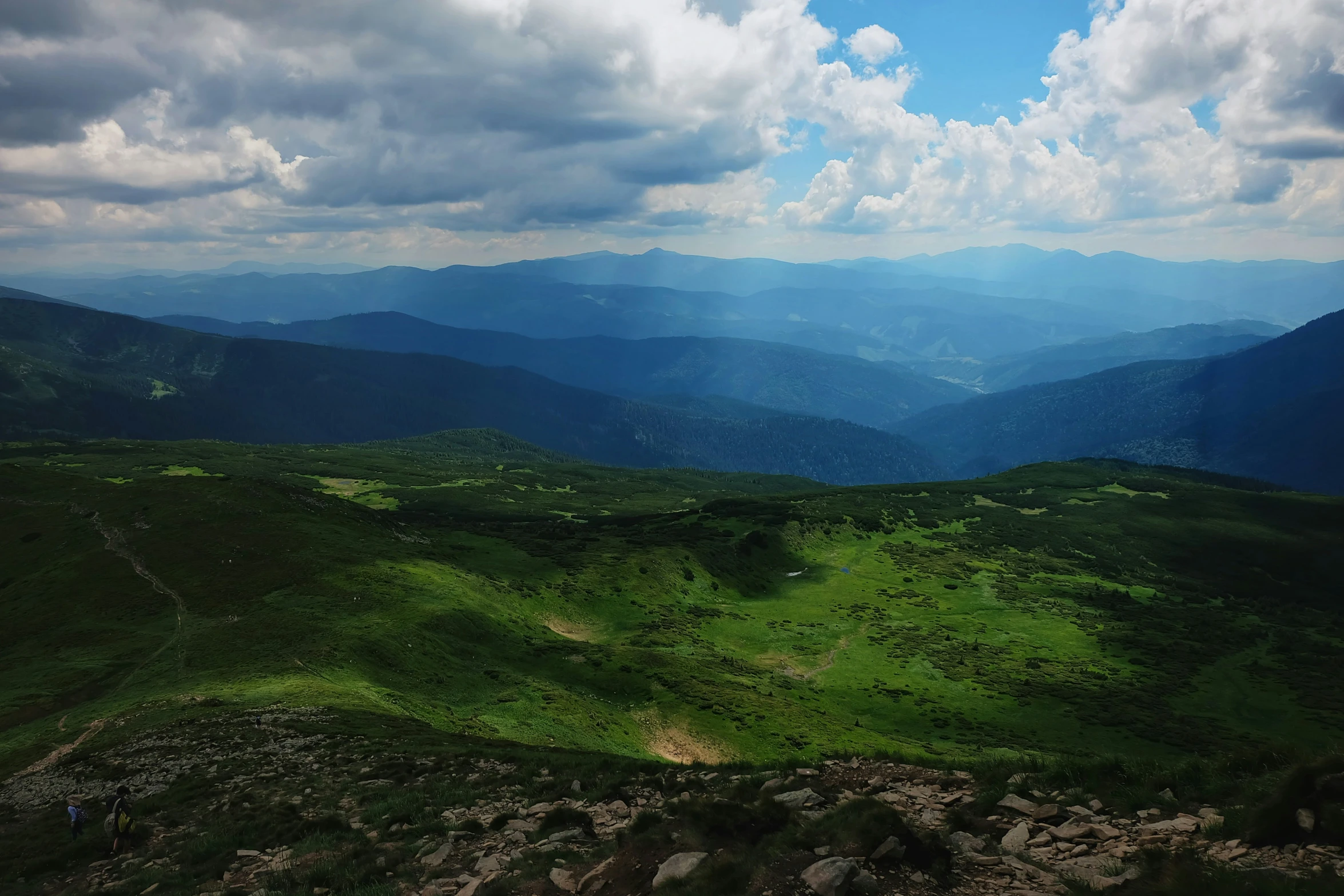 a green valley on the edge of a mountain with a cloudy sky