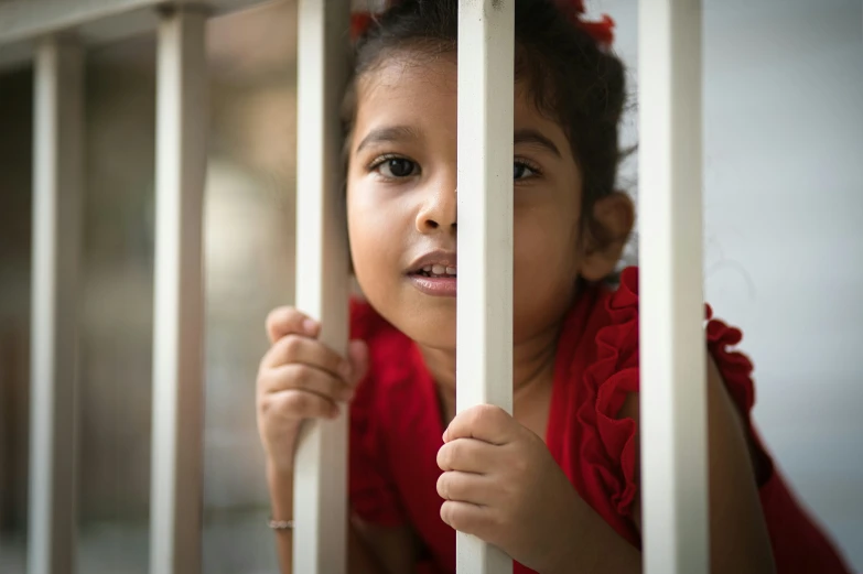 a little girl with red dress behind bars