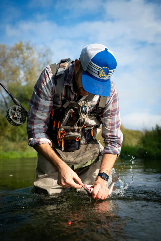 man crouched over while fly fishing with blue hat