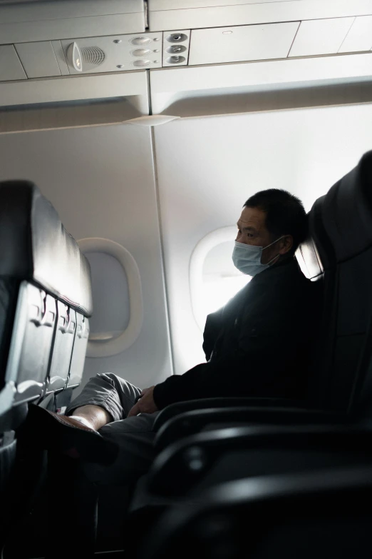 a man sitting in the aisle of an airplane wearing a mask