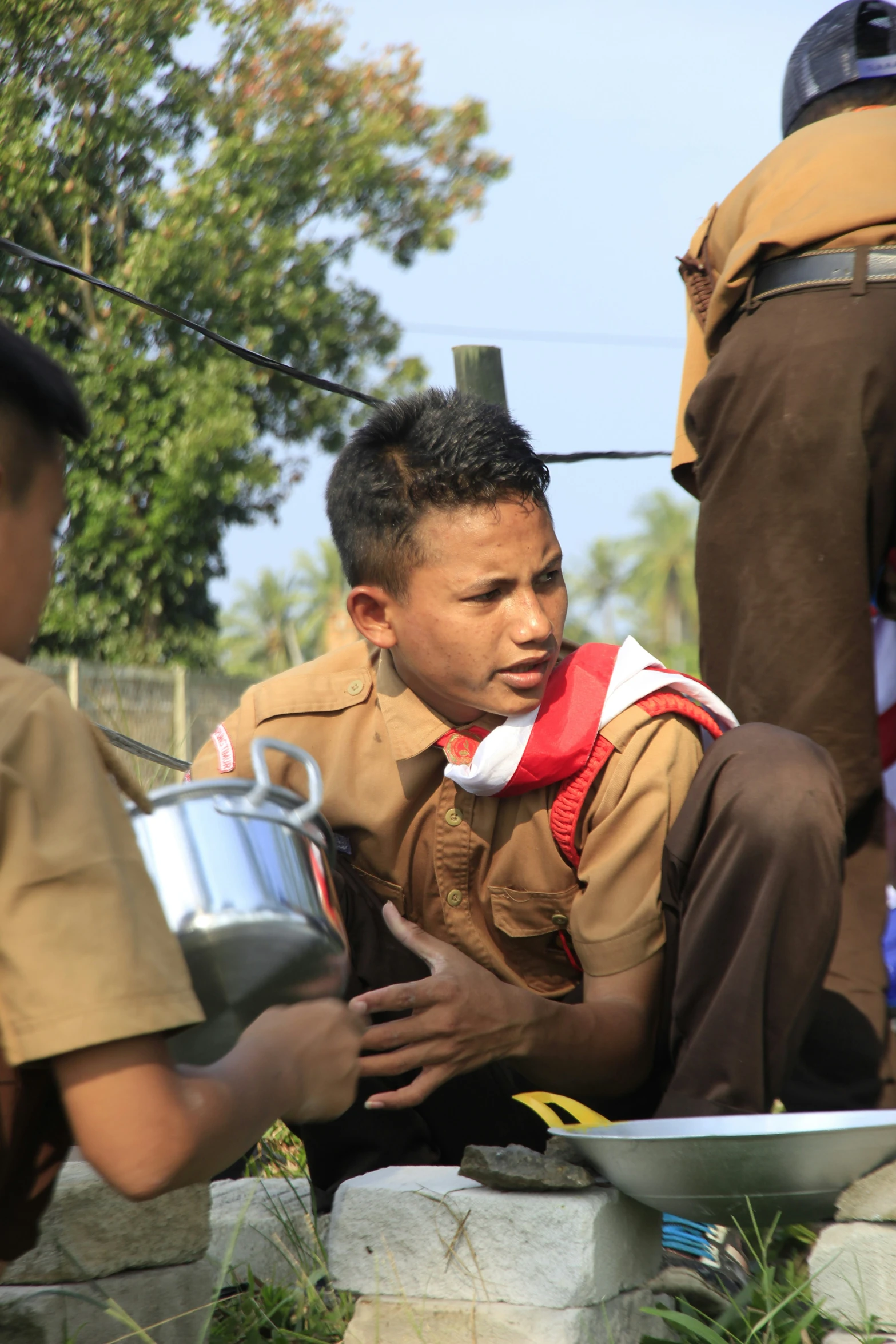 a boy in uniform sitting on rocks, holding a can