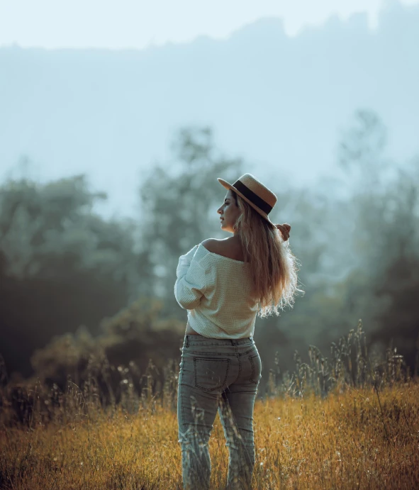 a beautiful woman standing in a field wearing a hat