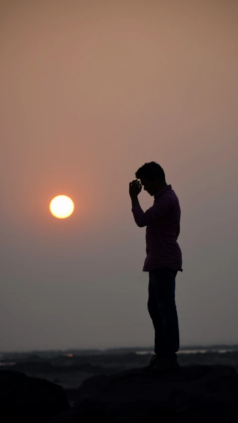 a person standing on the rocks near a body of water at sunset