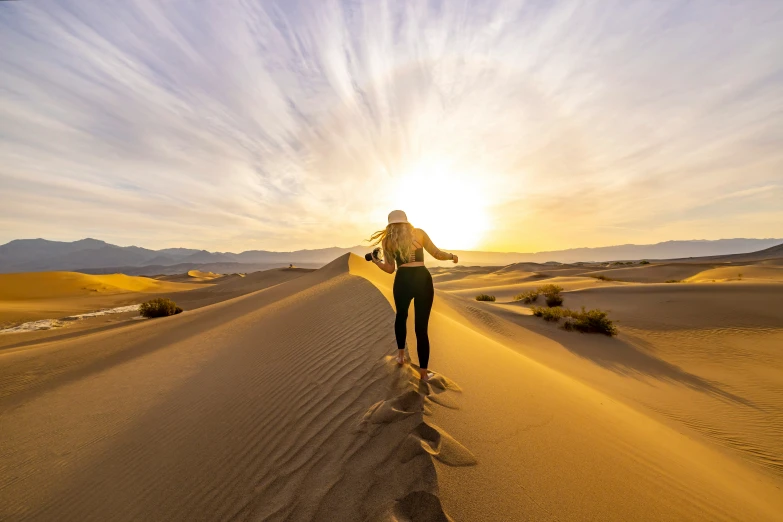 a woman in black clothing walking on sand dune