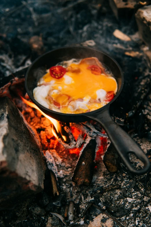 a bowl on a stove with bacon, eggs and a drink