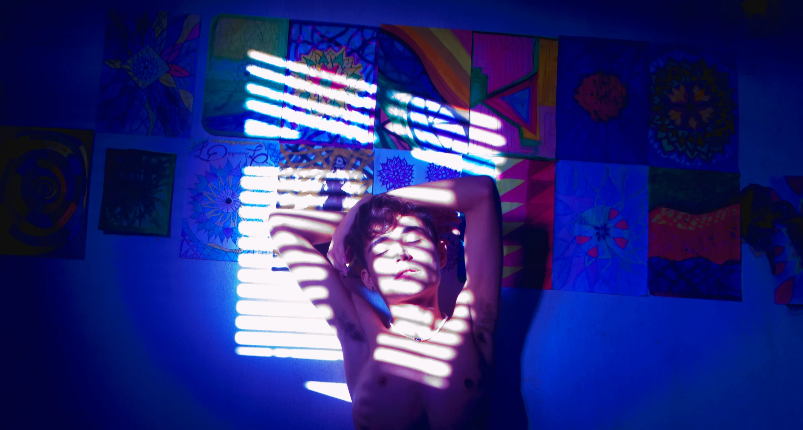 a woman posing in front of colorful art with her hands behind her head