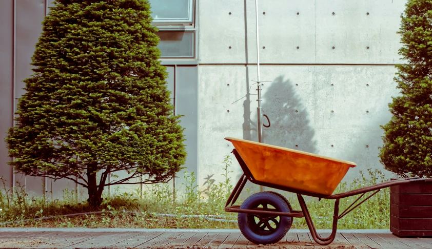 a wheelbarrow with an orange seat sitting next to shrubbery