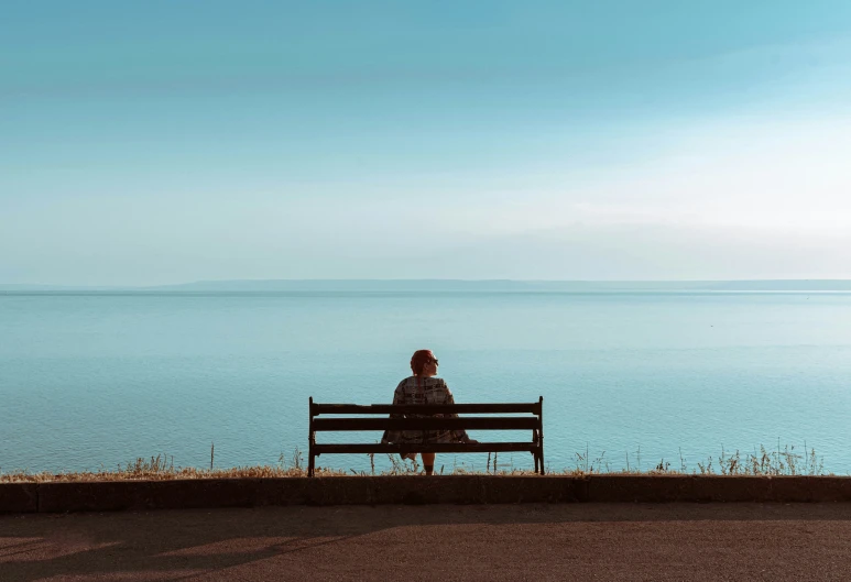 the lone person sits alone on the bench and watches the water