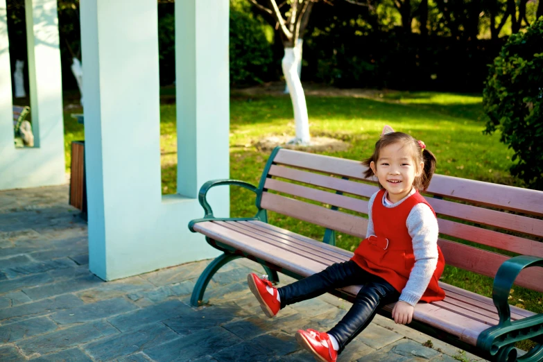 a little girl sitting on top of a wooden bench