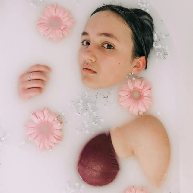 a woman laying in a bubble bath filled with pink flowers