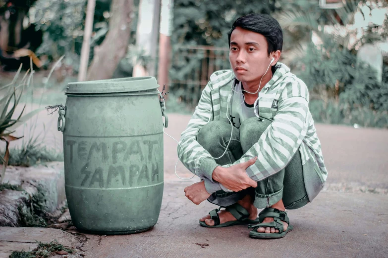 a man squatting near a green trash can