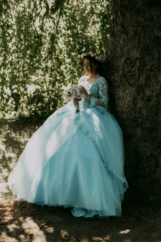 a  is wearing a long ball gown by a tree