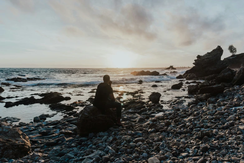 a man sitting on a rocky beach while looking at the water