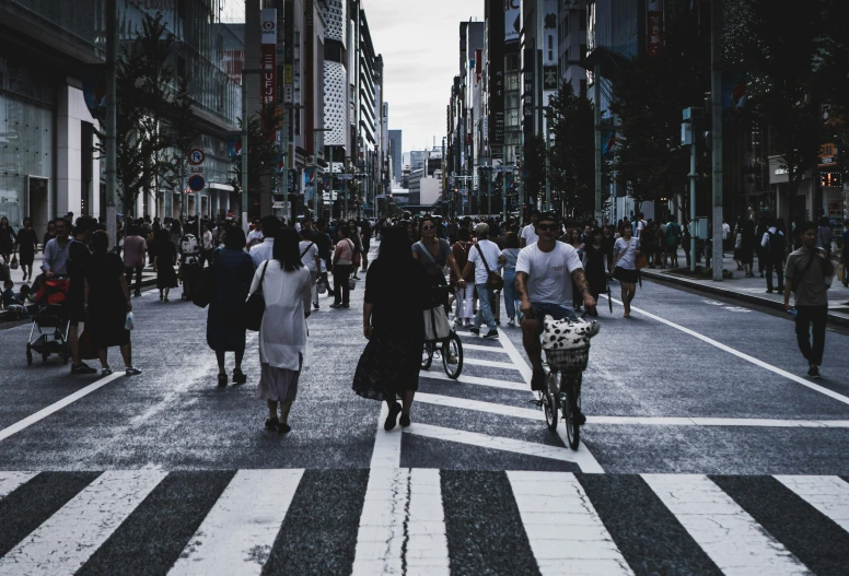 people walking and riding bikes in a cross walk with tall buildings