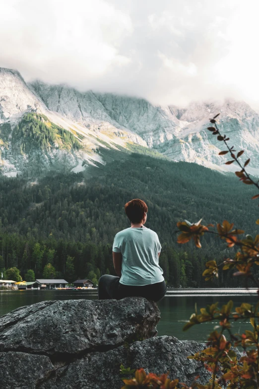 a boy sits on a rock looking out over a body of water