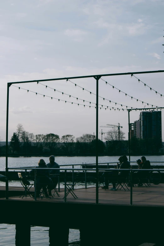 people sitting at tables near the water under strings of lights