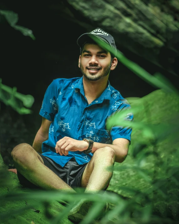 a man wearing a hat sitting on a rock in the woods