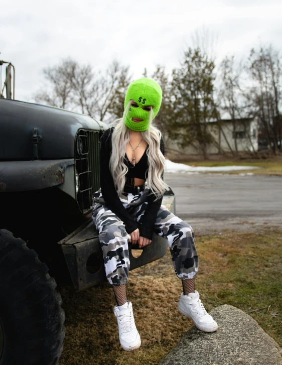 woman in camo pants and green hat sitting in front of truck