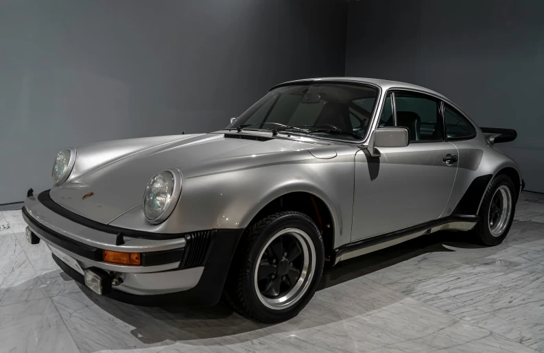 a silver porsche sits parked in a grey and black room