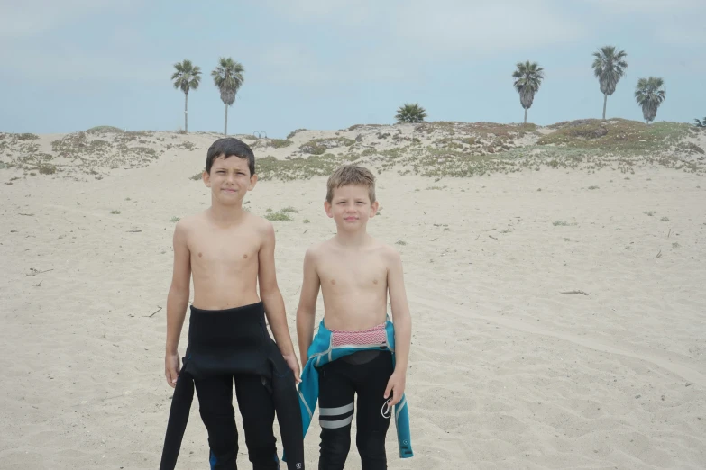 two boys are on a beach, in their wet suits