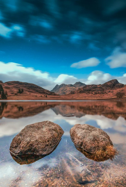 two rocks are in shallow water near the mountains