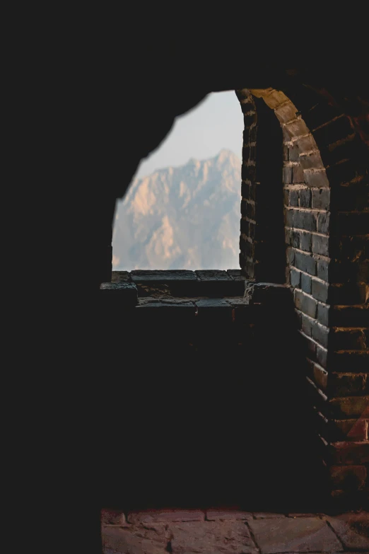 a window in a brick wall, with mountains in the distance