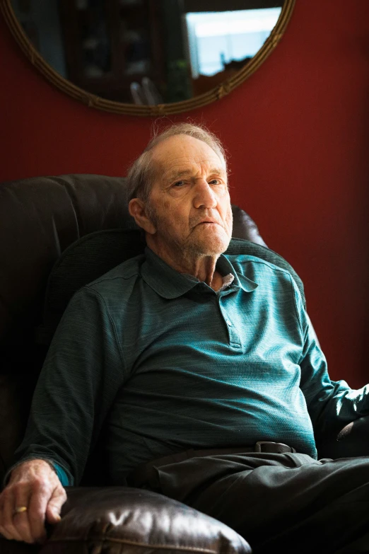 an elderly man sitting in a chair with his hand on his chin