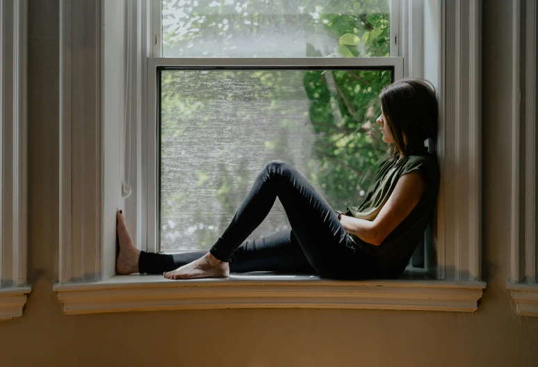 a woman is sitting on the window sill while looking outside