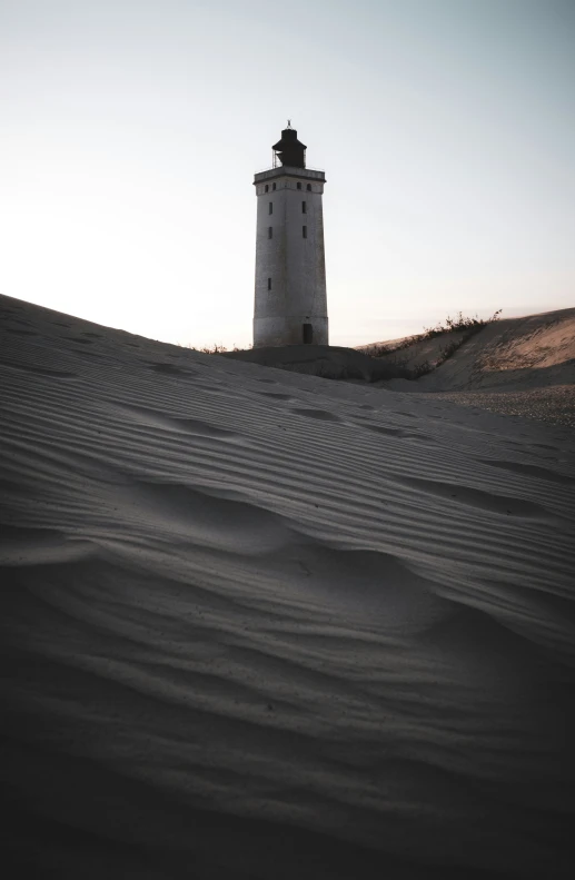 a white lighthouse sits atop the sand dunes