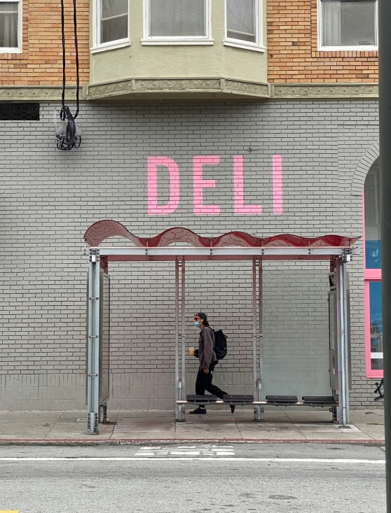 a man walks past a storefront that has pink lettering