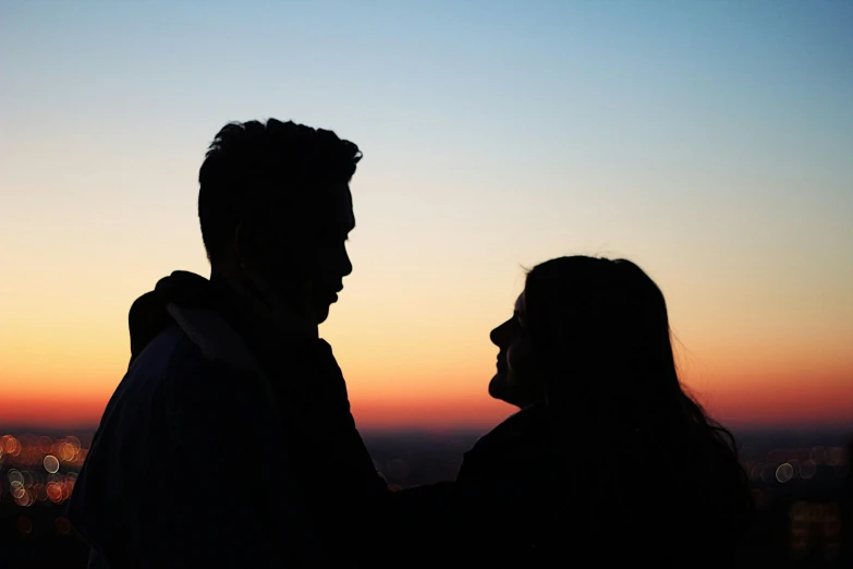 a silhouette of a man holding the arm of a woman while standing against a sunset