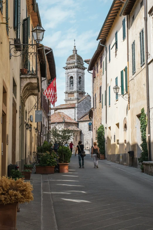 people walking in a village, with a church steeple in the background