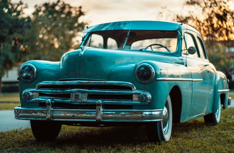 the classic car sits in the grass near a tree