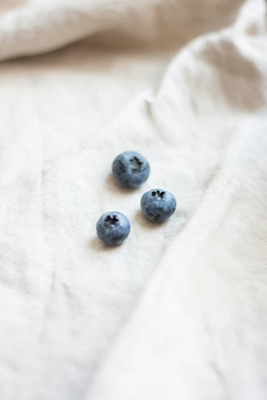 three blueberries on a bed and two scattered white sheets