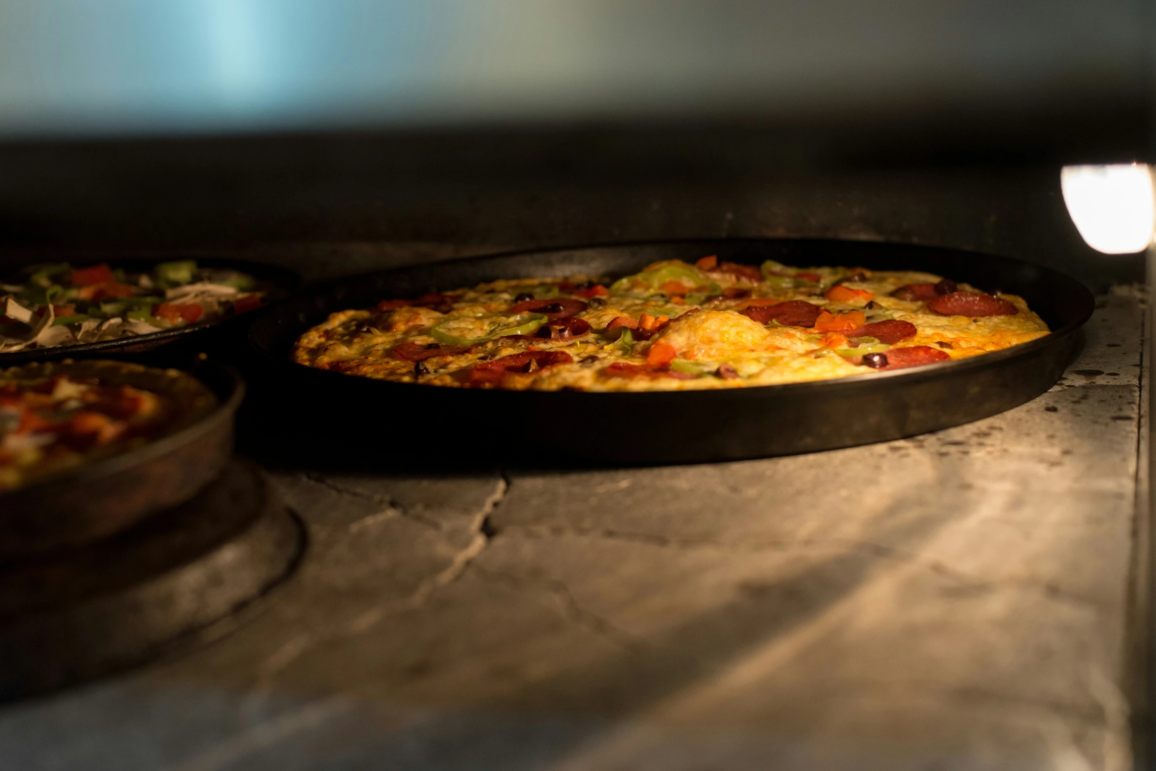 two pizzas with different toppings cooking in an oven